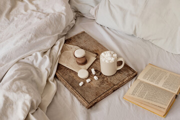 coffee with marshmallows and macaroons on a wooden tray, in bed. Aesthetically beautiful frame. Desserts in bed. hot chocolate with marshmallows. Cozy and warm day in bed