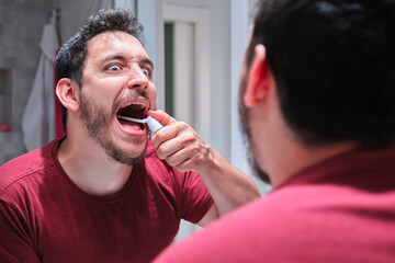 Man in pain while using a spray to treat an aphthae or sore on his throat.
