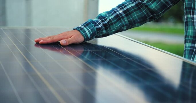 A man holds his hand above the surface of the sun panels. Close up of an young engineer hand is checking an operation of sun and cleanliness of photovoltaic solar panels on a sunset. 