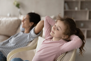 Happy calm little ethnic girl child and young Hispanic mother relax in armchair sleep or take nap...