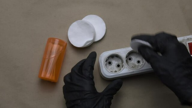 POV hands in black rubber gloves clean dirty plastic extension socket using cotton pads and cotton buds. Cleaning and maintenance of electric extender equipment