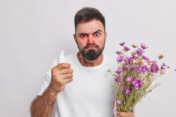 Hay fever symptoms. Displeased bearded adult European man holds aerosol to cure allergic reaction...