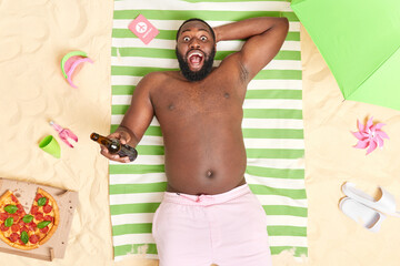 Top view of dark skinned Afro American man with thick beard holds bottle of beer has beach vacation...