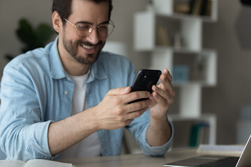 Happy businessman sit at desk distracted from work holding in hands smartphone smiling share...