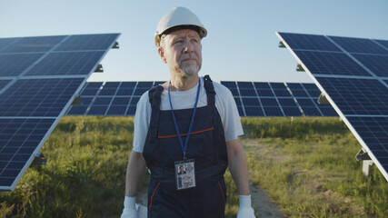 Adult man engineer technician standing against modern solar battery panels on green sunny field....