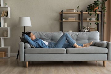 Side view woman enjoy day nap on comfy sofa. Young caucasian female put hands behind hear lying on...
