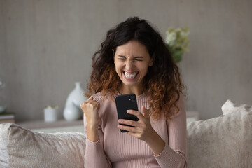 Overjoyed millennial Hispanic woman feel euphoric win online lottery on cellphone. Smiling young Latino female triumph read good news or get promotion notice on smartphone. Success concept.
