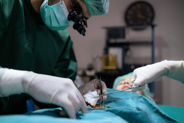Group of professional doctor wearing uniform and face mask doing surgery in the hospital in the operating room under light. Doctor using scisor and forceps to help patient. Medical health and cure