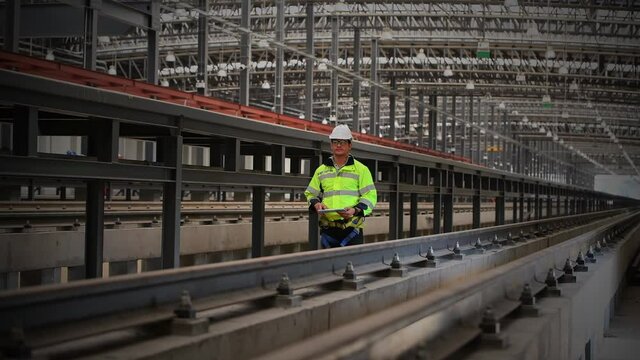 engineer under inspection and checking construction process railway work on rail train station by Blueprint on hand . Engineer wearing safety uniform and safety helmet in work.