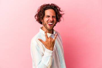 Young caucasian man isolated on pink bakcground showing rock gesture with fingers