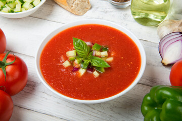 Gazpacho. Traditional Spanish tomato soup with fresh tomatoes, cucumber, bell pepper and basil on a white rustic wooden table.