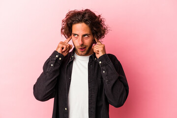 Young caucasian man isolated on pink bakcground covering ears with fingers, stressed and desperate by a loudly ambient.