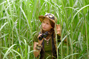 A young girl is dressed up as an explorer. She 
is seen in a tropical jungle environment 
observing...