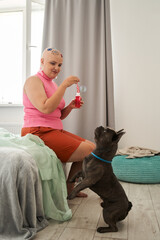 Bald lady holding bottle with soap water and blowing bubbles at home