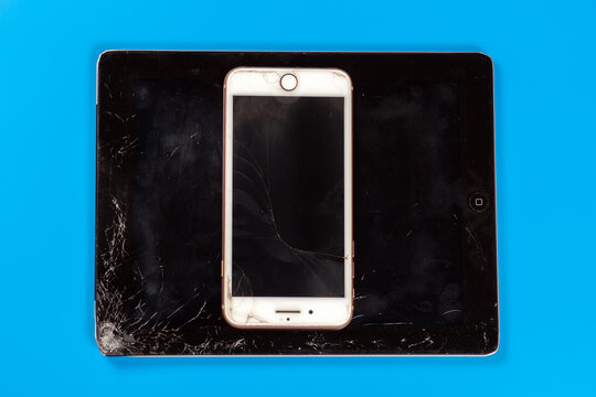 Tablet Computer Apple IPad And IPhone With Broken And Dirty Screen Glass. Result Of Falling Or Crash, Bad Condition Of Devices. Vibrant Blue Background, Copy Space.