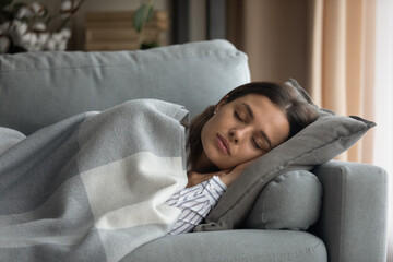 Beautiful serene woman sleeping on comfy sofa under warm cozy plaid in modern living room. Healthy...