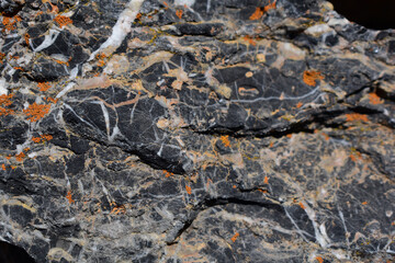 Schwarzer Kalkstein mit weißen Adern und gelb orangenen Flechten als Hintergrund in der Sonne copy space