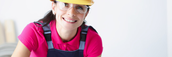 Smiling female construction worker in yellow helmet bent over blueprints