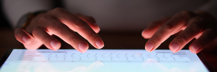 Female fingers are typing on tablet screen at night