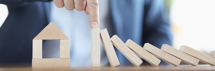 Businessman holds falling figurines of wooden blocks on house