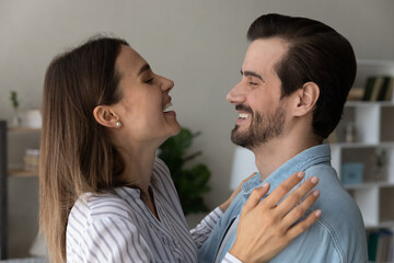 Side profile happy faces of overjoyed couple looking at each other laughing hugging at home. Festive mood, life events, relocation at new own first house celebration. Love and romantic date concept