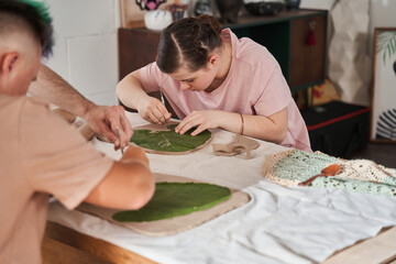 Girl attentively making impression of the leaf texture to the clay at the master class