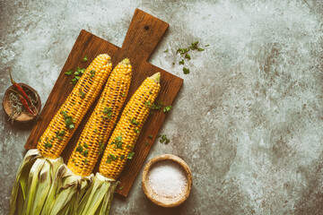 Grilled sweet corn cobs on a wooden cutting board, dark grunge background. Vegan and vegetarian...