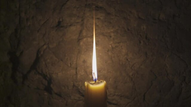 yellow candle in dark cave calm with burning candle flame on night peace and stone wall background for warm white light and holy thing with pray at temple or church on slow motion