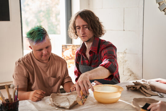Boy with special needs sitting at table with professional sculptor and looking at plate
