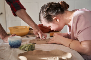 Girl carefully making plate from the clay under supervision of the mentor