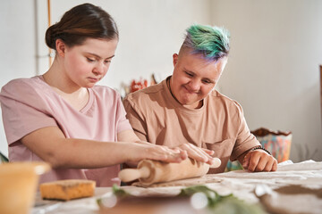 Girl with down syndrome rolling out with the pin different shapes from the clay