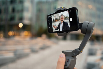 Confident blogger male manager of European appearance gray-haired conference. Records video on the phone and conducts an online broadcast with clients. Good mood businessman.