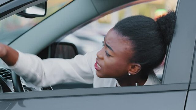 Young afro american girl driver stressed african ethnic woman sitting in car in traffic jam screaming swears angry with slow transportation on road emotionally waving hands with problems with driving