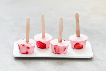 Mini strawberry ice cream on a wooden stick on a ceramic plate on a light background