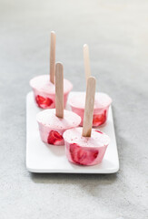 Fototapeta na wymiar Summer dessert strawberry ice cream on a wooden stick on a ceramic plate on a light background
