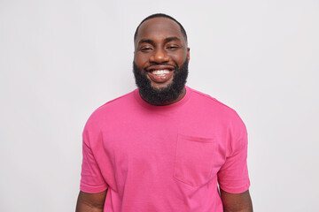 Photo of handsome dark skinned bearded man smiles happily at camera shows white perfect teeth has...