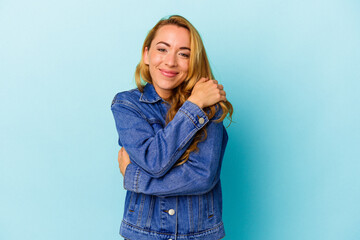 Caucasian woman isolated on blue background hugs, smiling carefree and happy.