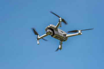 Flying drone with camera on a blue background with copy space. Airborne quadcopter. Also known as a...