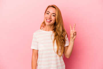 Caucasian blonde woman isolated on pink background joyful and carefree showing a peace symbol with fingers.