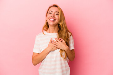 Caucasian blonde woman isolated on pink background laughing keeping hands on heart, concept of happiness.