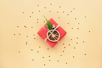 Red Christmas gift in a box with confetti on beige background. Top view, flat lay