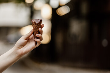 Sweet ice cream cone. A tasty, yummy, beautiful Chocolate ice cream.  Close up of women hand holding delicious ice cream waffle cone with chocolate and Cream, Blur background. Summer dessert. Walking