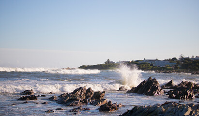 Ocean sunset view with vacation homes in the background and rocks in the foreground.