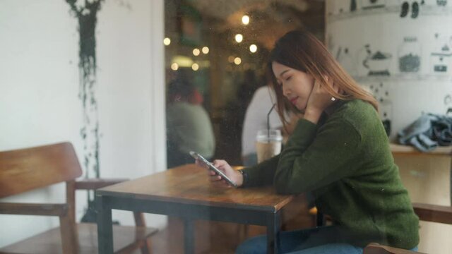 4K Beautiful Asian woman sitting in cafe using smartphone with internet for online shopping or social media. Modern female enjoy outdoor activity lifestyle with wireless technology and smart gadget