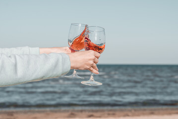 Two glasses of rose wine in female's hands against the sky and seashore.