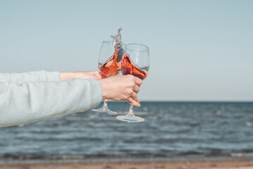 Two glasses of rose wine in female's hands against the sky and seashore. - obrazy, fototapety, plakaty
