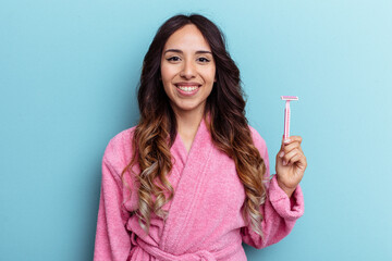 Young mexican woman wearing a bathrobe holding a knife isolated on blue background happy, smiling and cheerful.