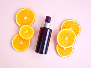 Mockup of unbranded brown plastic spray bottle and orange slices on light pink background. Natural organic cosmetics. Container for professional cosmetics product. Eco-friendly cosmetic products