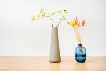 Decorative vases with colorful dried flower branches and yellow dried blueberries branches on oak floor and white background