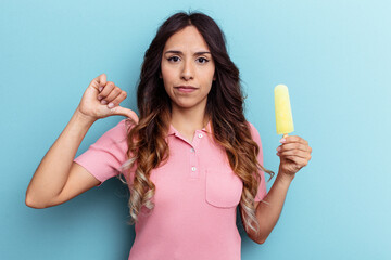 Young latin woman holding ice cream isolated on blue background showing a dislike gesture, thumbs...